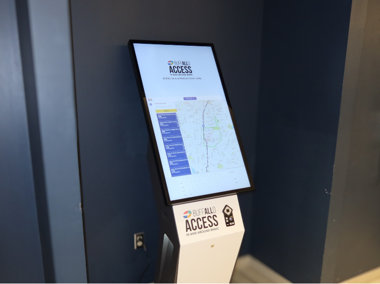The image shows a tall computer screen on a stand with the All Access Logo. The screen is a touch screen that will allow users to schedule a trip on the app